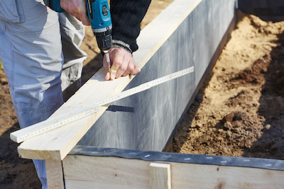 gardener screwing on wooden plank to build a raised bed