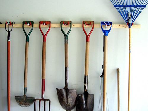 Various gardening tools like rakes, shovels, and pruning shears hanging neatly on a pegboard in a shed